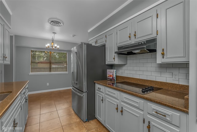 kitchen with black electric cooktop, decorative backsplash, light tile patterned flooring, stainless steel refrigerator, and a chandelier