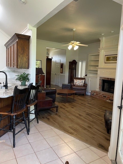 living room with sink, light wood-type flooring, crown molding, and a brick fireplace