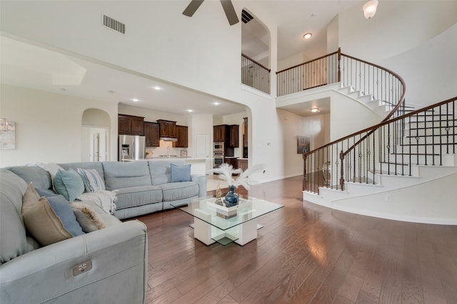 living room with ceiling fan, a towering ceiling, and dark hardwood / wood-style floors