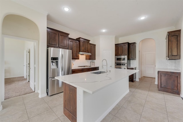 kitchen with light tile patterned floors, an island with sink, appliances with stainless steel finishes, dark brown cabinetry, and sink