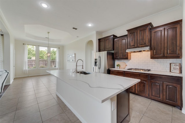 kitchen featuring an island with sink, appliances with stainless steel finishes, a tray ceiling, light tile patterned flooring, and sink