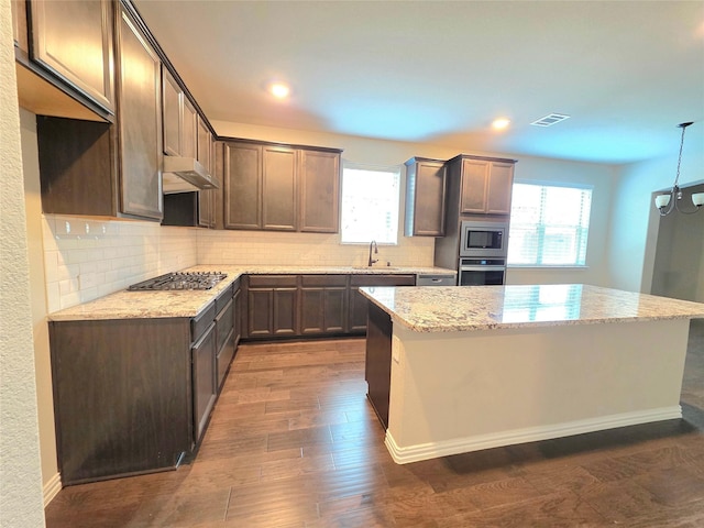 1516 Fairweather Way, Forney, TX 75126 - kitchen with under cabinet range hood, appliances with stainless steel finishes, light stone countertops, a center island, and tasteful backsplash