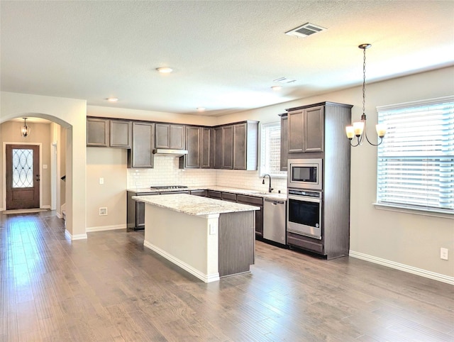 1516 Fairweather Way, Forney, TX 75126 - kitchen featuring appliances with stainless steel finishes, a chandelier, a center island, arched walkways, and decorative backsplash