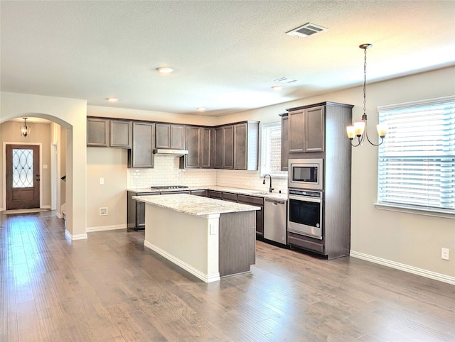 kitchen with light stone counters, a chandelier, hanging light fixtures, appliances with stainless steel finishes, and a kitchen island