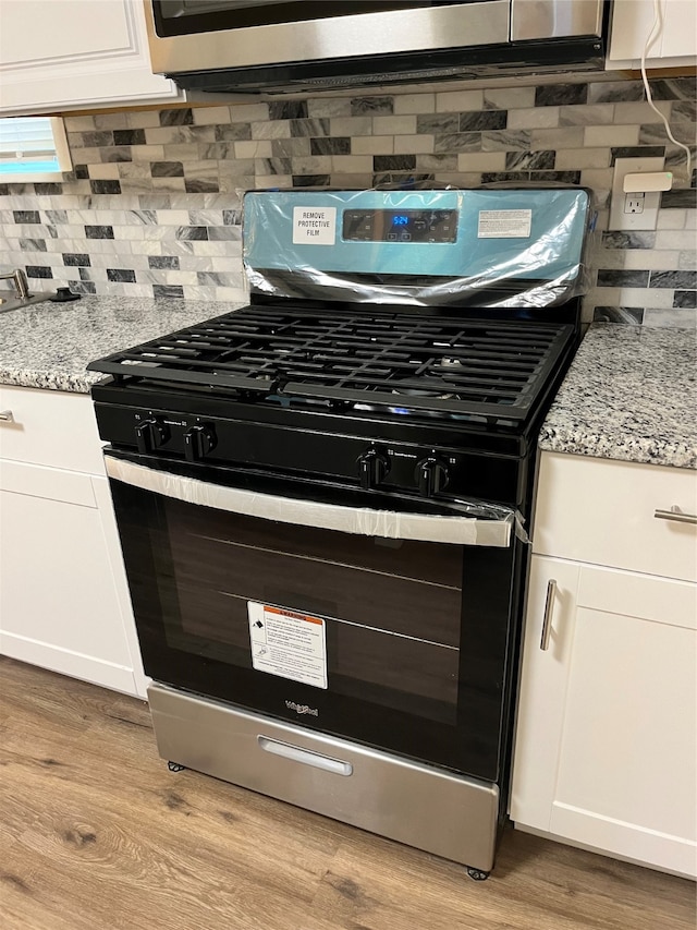 details with light wood-type flooring, decorative backsplash, stainless steel appliances, and white cabinets