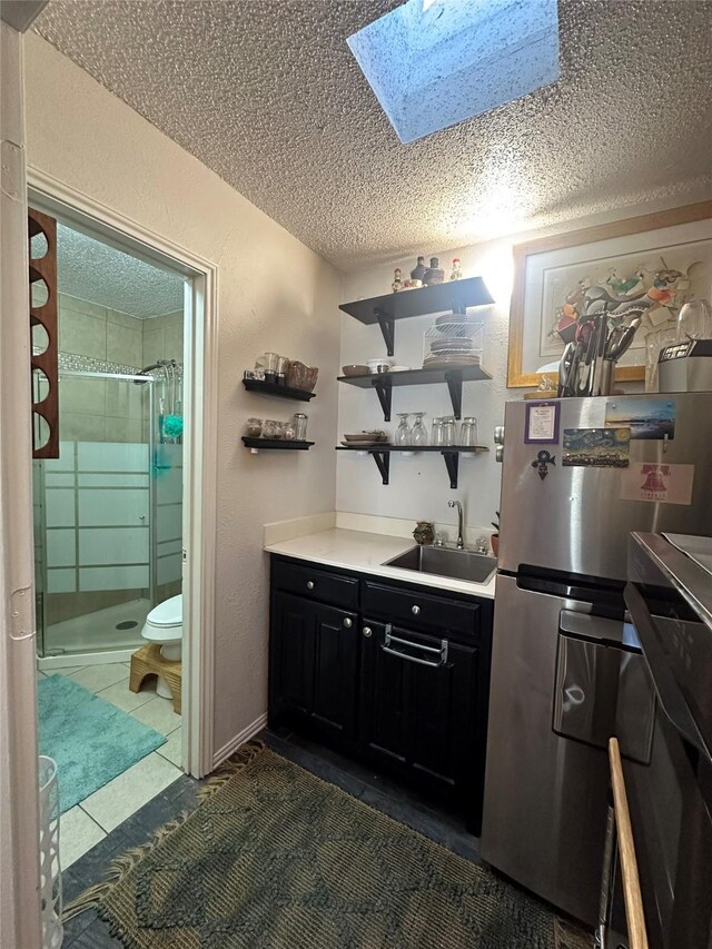 kitchen featuring a textured ceiling, dark tile patterned floors, sink, and stainless steel refrigerator