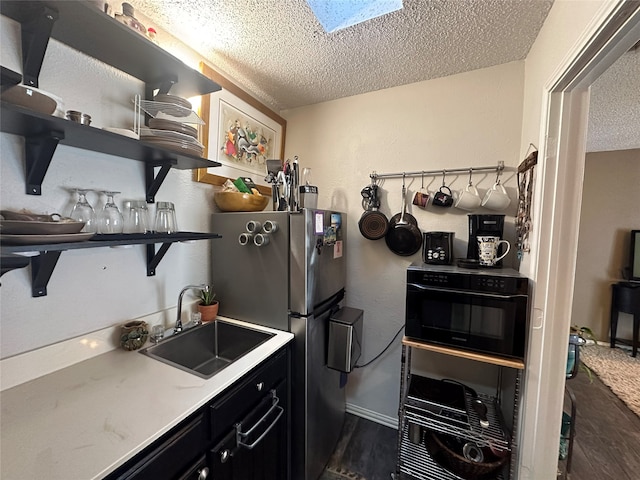 kitchen featuring stainless steel refrigerator, a skylight, sink, and a textured ceiling