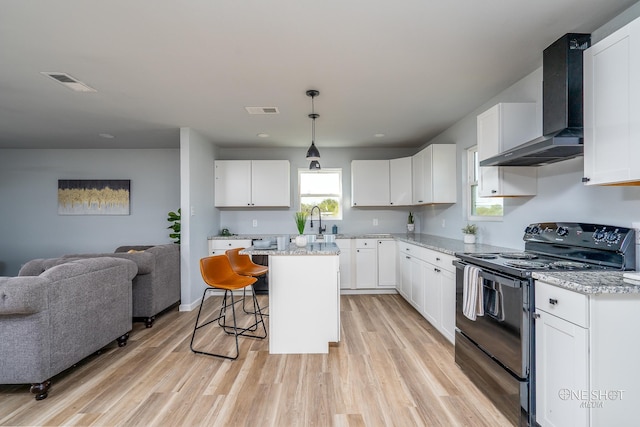 kitchen featuring white cabinets, wall chimney exhaust hood, black electric range, a kitchen island, and a breakfast bar area