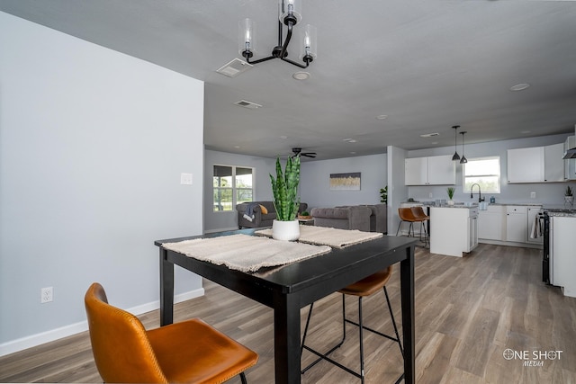 dining space with hardwood / wood-style flooring, plenty of natural light, sink, and ceiling fan with notable chandelier