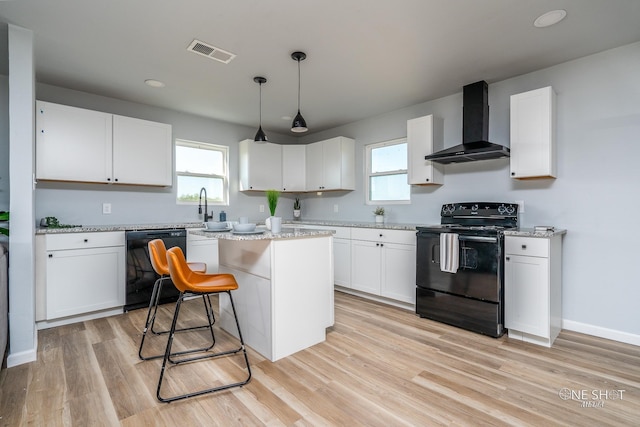 kitchen featuring white cabinetry, wall chimney exhaust hood, pendant lighting, a kitchen island, and black appliances