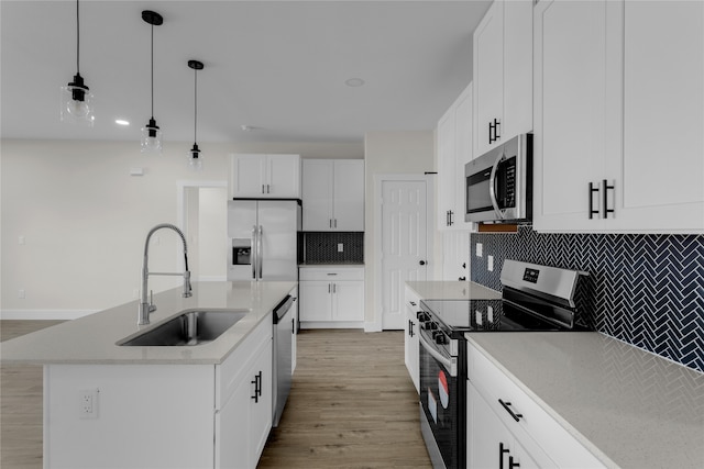 kitchen featuring an island with sink, sink, decorative light fixtures, white cabinetry, and appliances with stainless steel finishes