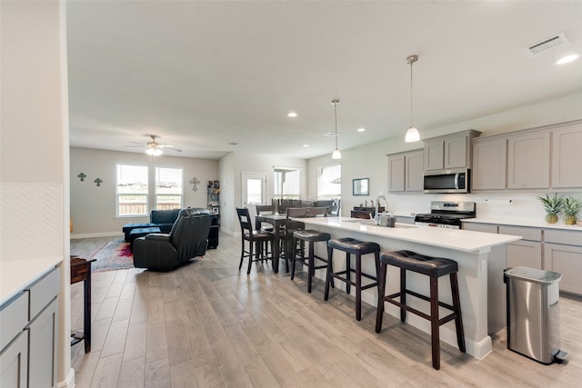 kitchen with ceiling fan, stainless steel appliances, light hardwood / wood-style floors, and a breakfast bar