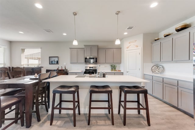 kitchen with pendant lighting, an island with sink, light hardwood / wood-style flooring, gray cabinetry, and appliances with stainless steel finishes