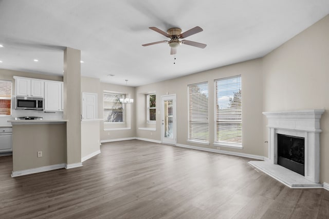 unfurnished living room with a healthy amount of sunlight, ceiling fan with notable chandelier, and dark hardwood / wood-style floors