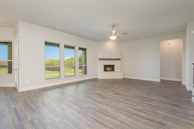 unfurnished living room featuring ceiling fan, a stone fireplace, and dark wood-type flooring