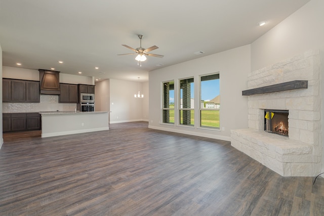 unfurnished living room featuring ceiling fan with notable chandelier, a stone fireplace, and dark hardwood / wood-style floors