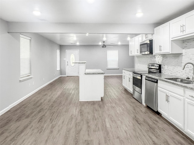 kitchen with sink, white cabinetry, light wood-type flooring, appliances with stainless steel finishes, and light stone countertops