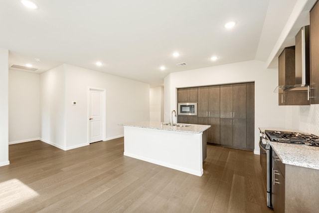 kitchen featuring a center island with sink, sink, hardwood / wood-style flooring, light stone countertops, and stainless steel appliances