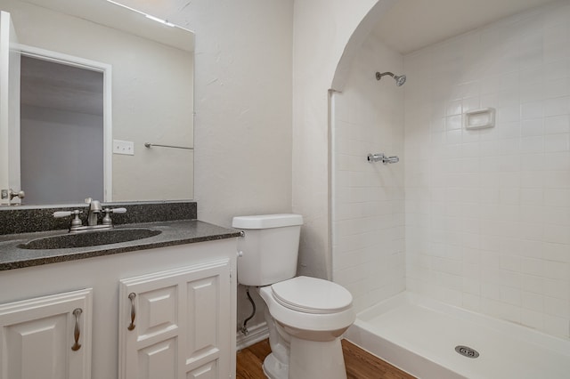 bathroom featuring wood-type flooring, tiled shower, vanity, and toilet