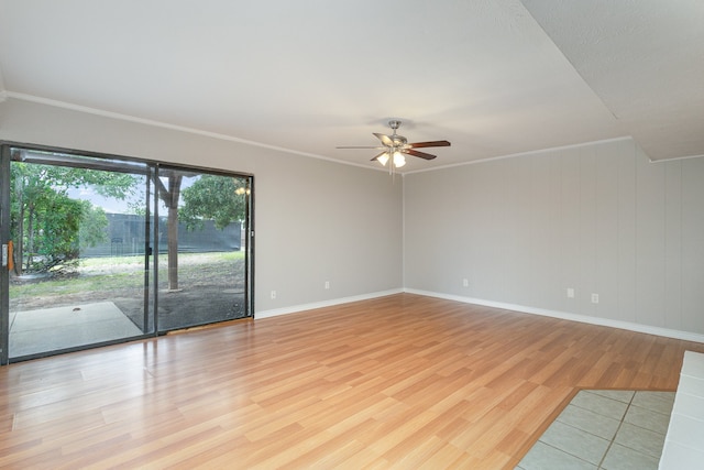 spare room with ornamental molding, light wood-type flooring, wood walls, and ceiling fan