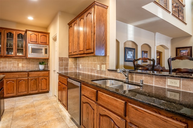 kitchen featuring light tile patterned floors, sink, appliances with stainless steel finishes, dark stone countertops, and decorative backsplash