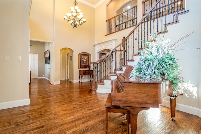 foyer entrance featuring wood-type flooring, an inviting chandelier, crown molding, and a high ceiling