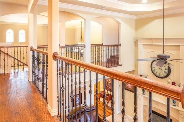 corridor with wood-type flooring, a tray ceiling, crown molding, and a chandelier