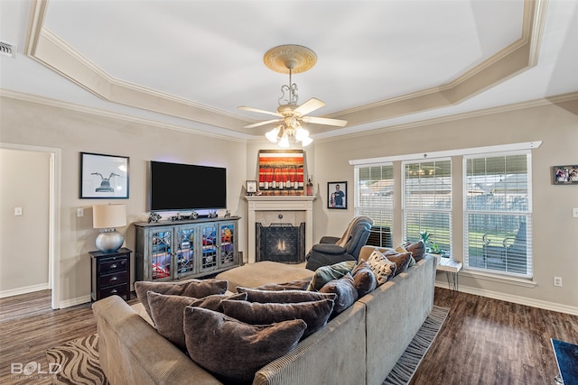 living room with ceiling fan, ornamental molding, a raised ceiling, and dark wood-type flooring