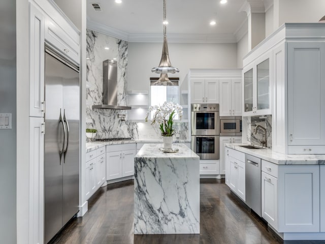 kitchen with a center island, built in appliances, white cabinets, wall chimney exhaust hood, and light stone countertops