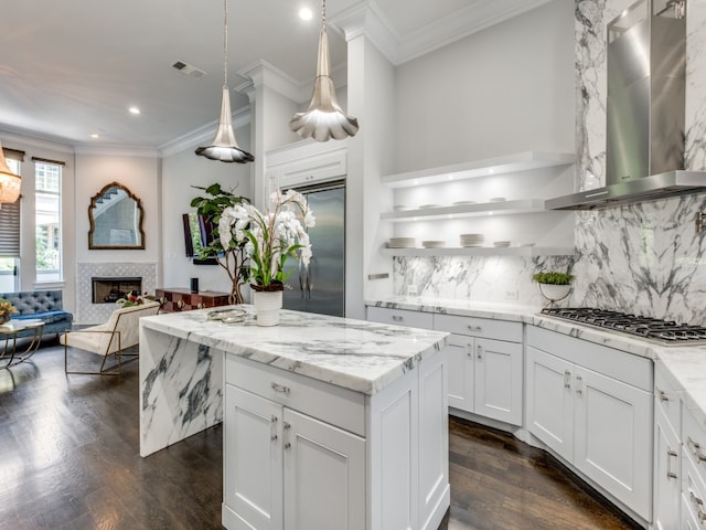 kitchen featuring appliances with stainless steel finishes, dark wood-type flooring, white cabinets, a tile fireplace, and wall chimney range hood