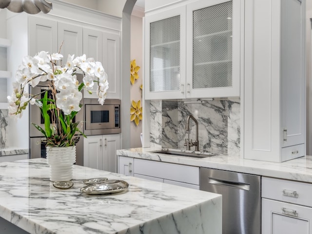 interior space with appliances with stainless steel finishes, light stone counters, white cabinets, tasteful backsplash, and sink