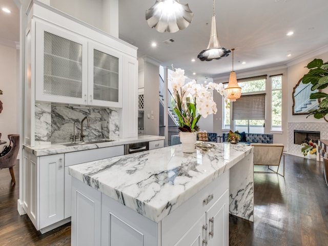 kitchen featuring pendant lighting, a center island, a tile fireplace, white cabinets, and decorative backsplash