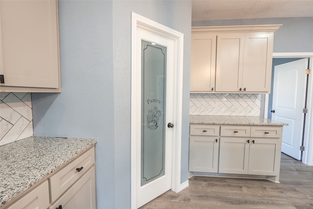 kitchen featuring backsplash, cream cabinets, light hardwood / wood-style flooring, and light stone counters