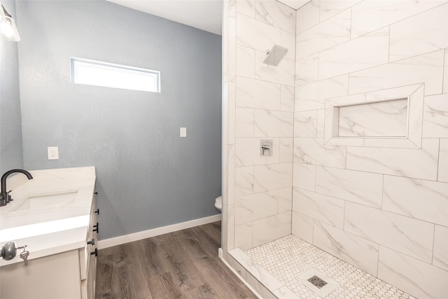 bathroom with a tile shower, hardwood / wood-style flooring, vanity, and toilet