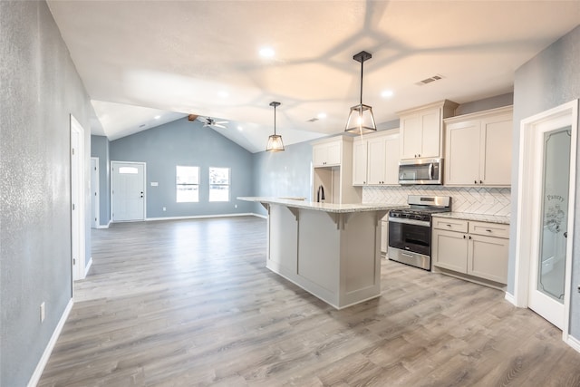 kitchen featuring stainless steel appliances, light wood-type flooring, ceiling fan, decorative light fixtures, and a center island with sink