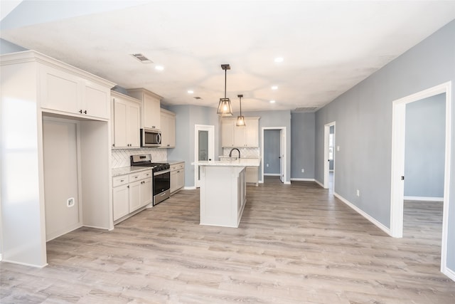 kitchen featuring light wood-type flooring, a kitchen island with sink, hanging light fixtures, stainless steel appliances, and light stone countertops