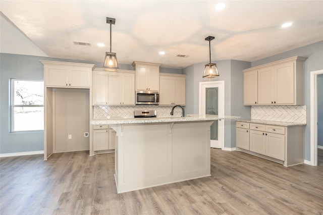 kitchen with light hardwood / wood-style flooring, a center island with sink, appliances with stainless steel finishes, and decorative light fixtures