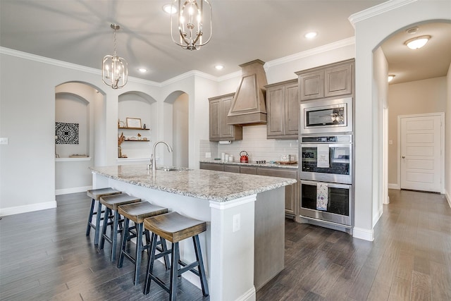 kitchen with a kitchen island with sink, sink, a notable chandelier, hanging light fixtures, and dark hardwood / wood-style flooring