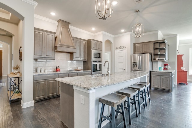 kitchen with a chandelier, dark wood-type flooring, a kitchen island with sink, custom range hood, and appliances with stainless steel finishes