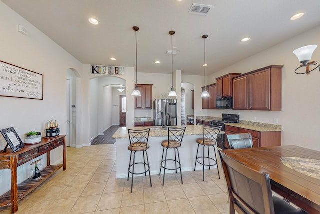 kitchen with a kitchen island with sink, black appliances, light stone countertops, and pendant lighting