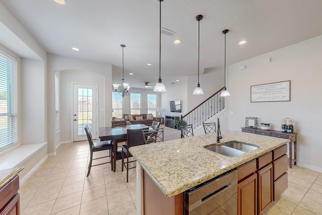 kitchen with an island with sink, light stone countertops, dishwasher, decorative light fixtures, and sink