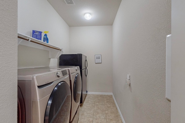 clothes washing area with light tile patterned floors, a textured ceiling, and washer and clothes dryer