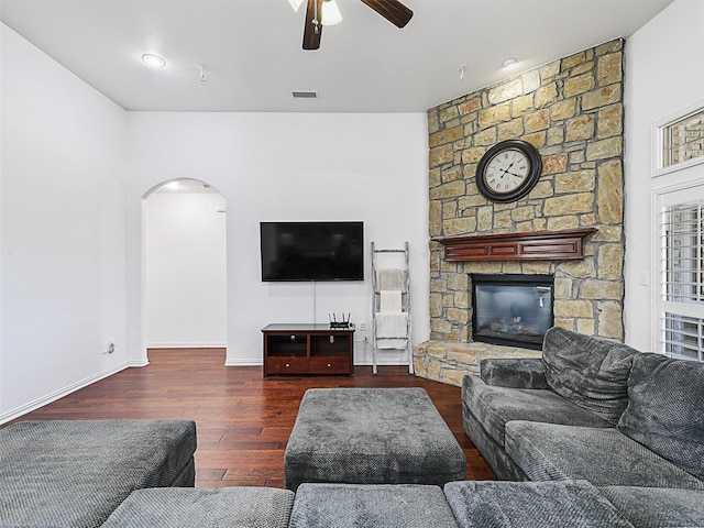 living room with ceiling fan, a stone fireplace, and dark wood-type flooring