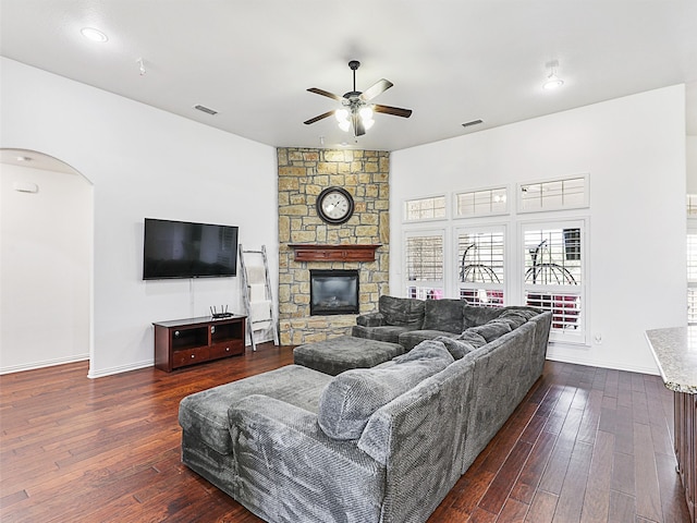 living room with a stone fireplace, dark hardwood / wood-style flooring, and ceiling fan