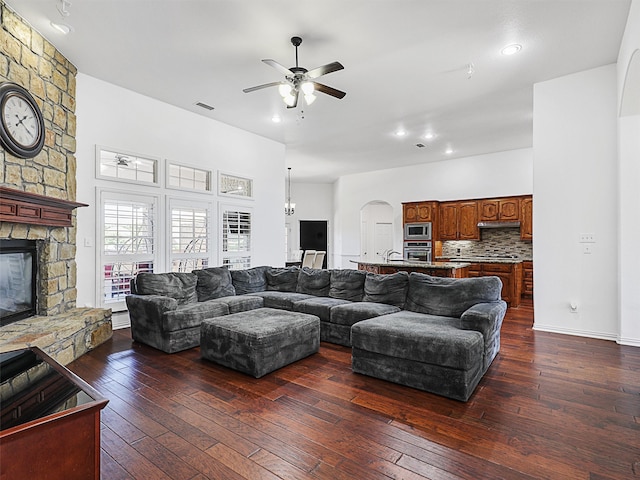 living room featuring a stone fireplace, dark wood-type flooring, and ceiling fan