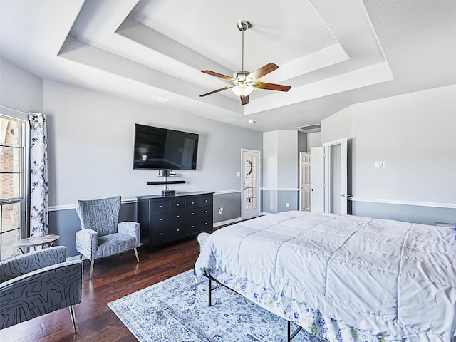 bedroom featuring ceiling fan, a tray ceiling, and dark wood-type flooring