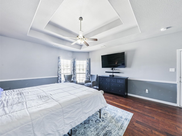 bedroom featuring a textured ceiling, a tray ceiling, dark hardwood / wood-style flooring, and ceiling fan