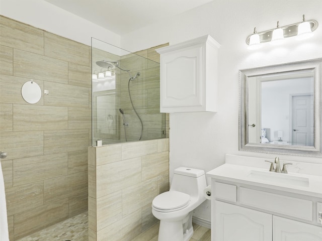 bathroom featuring a tile shower, vanity, and toilet