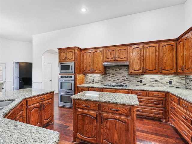 kitchen featuring light stone counters, backsplash, stainless steel appliances, dark hardwood / wood-style floors, and a center island