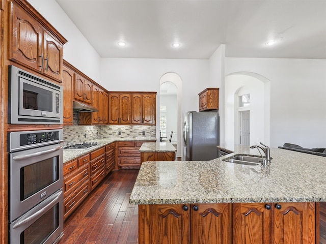 kitchen with dark hardwood / wood-style floors, a kitchen island with sink, sink, decorative backsplash, and stainless steel appliances